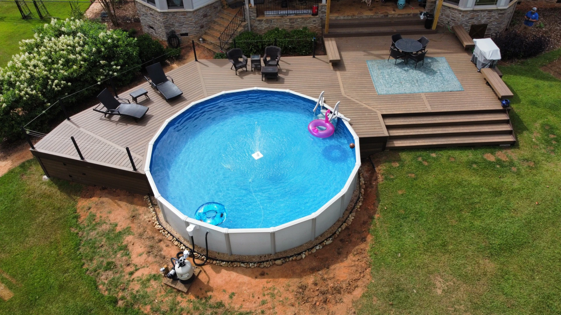 Above ground pool with wraparound deck, lounge chairs, and outdoor dining area.
