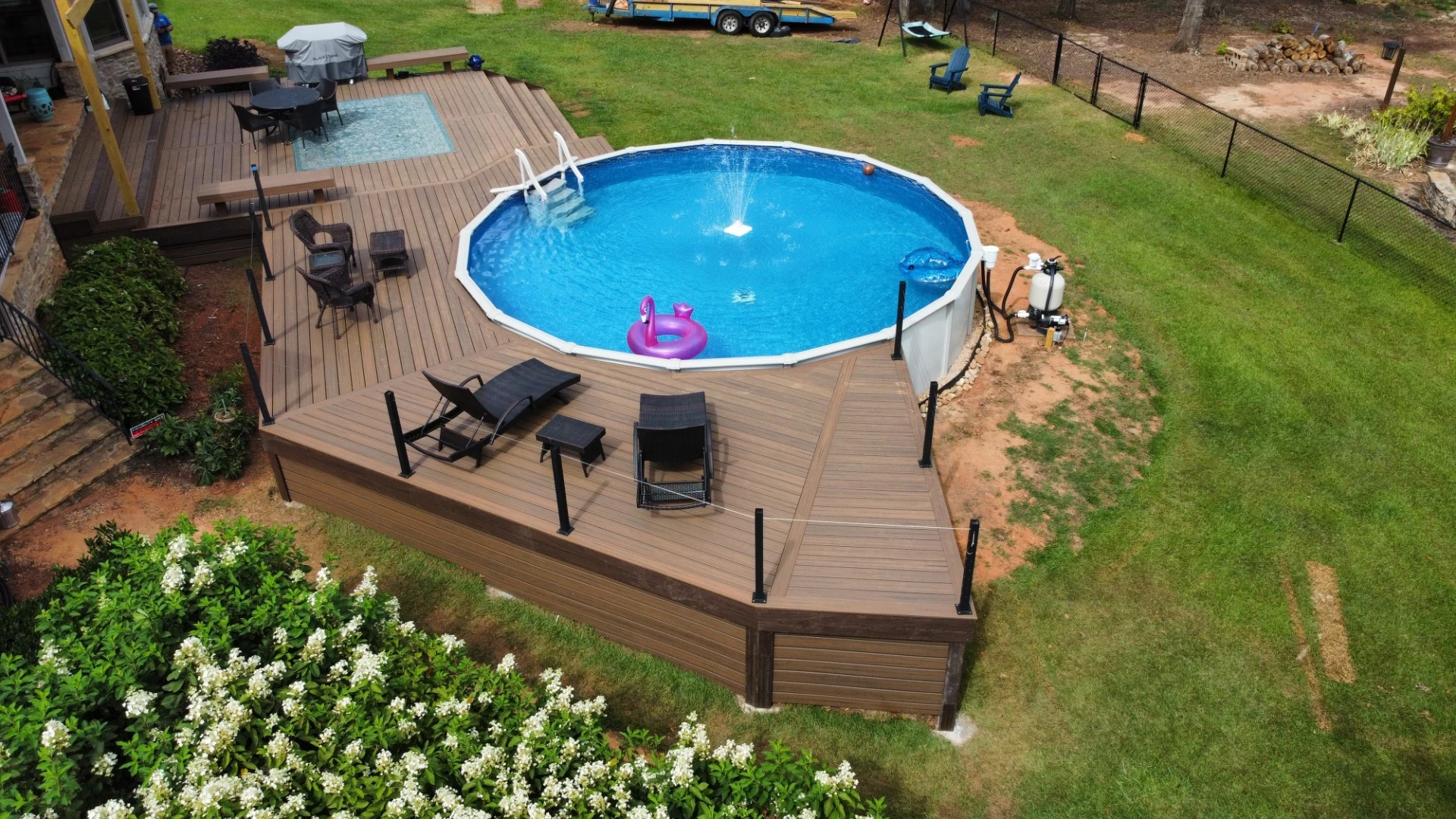 Angled aerial view of pool deck with lounge chairs and backyard.