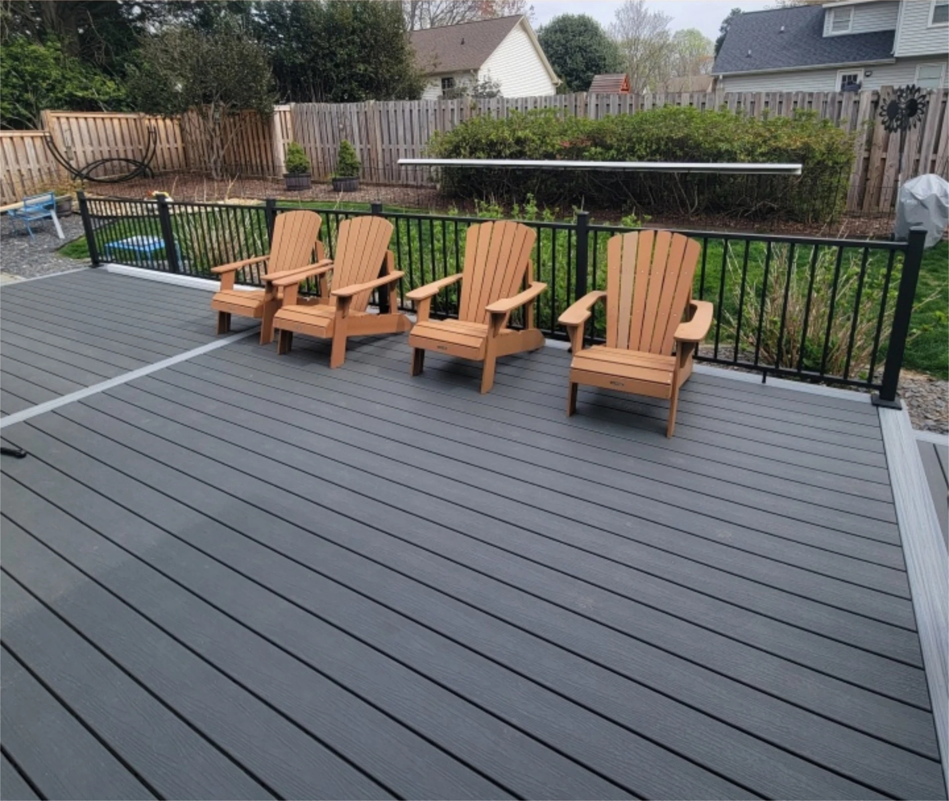 Backyard deck with four Adirondack chairs by a black railing.