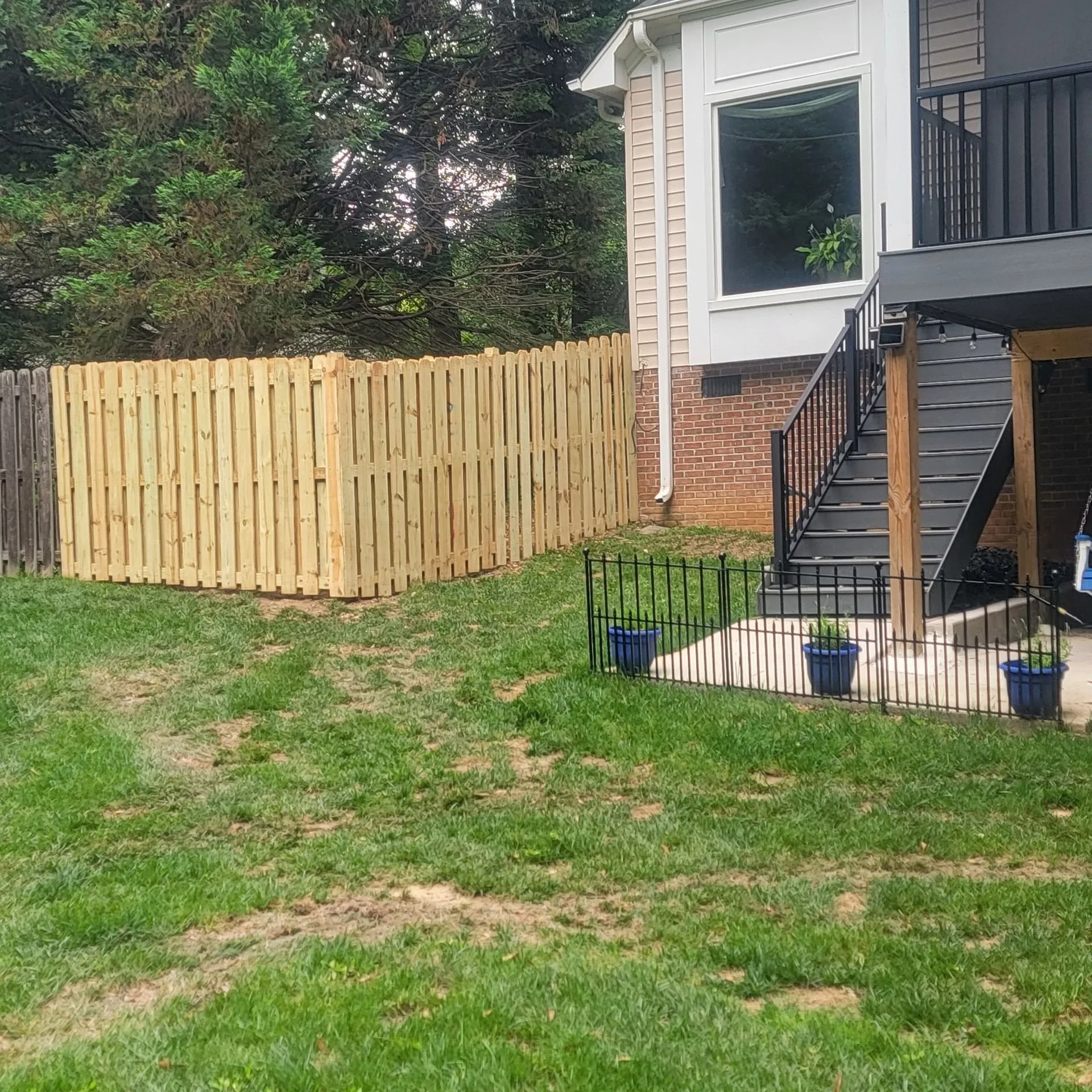 Backyard with new wooden privacy fence beside raised deck stairs.