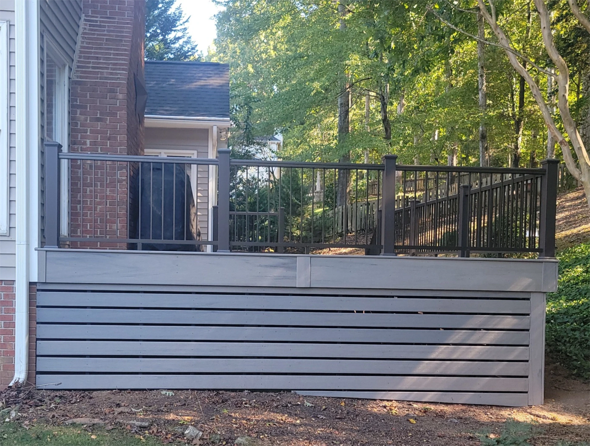 Elevated backyard deck with black metal railing and gray horizontal skirting.