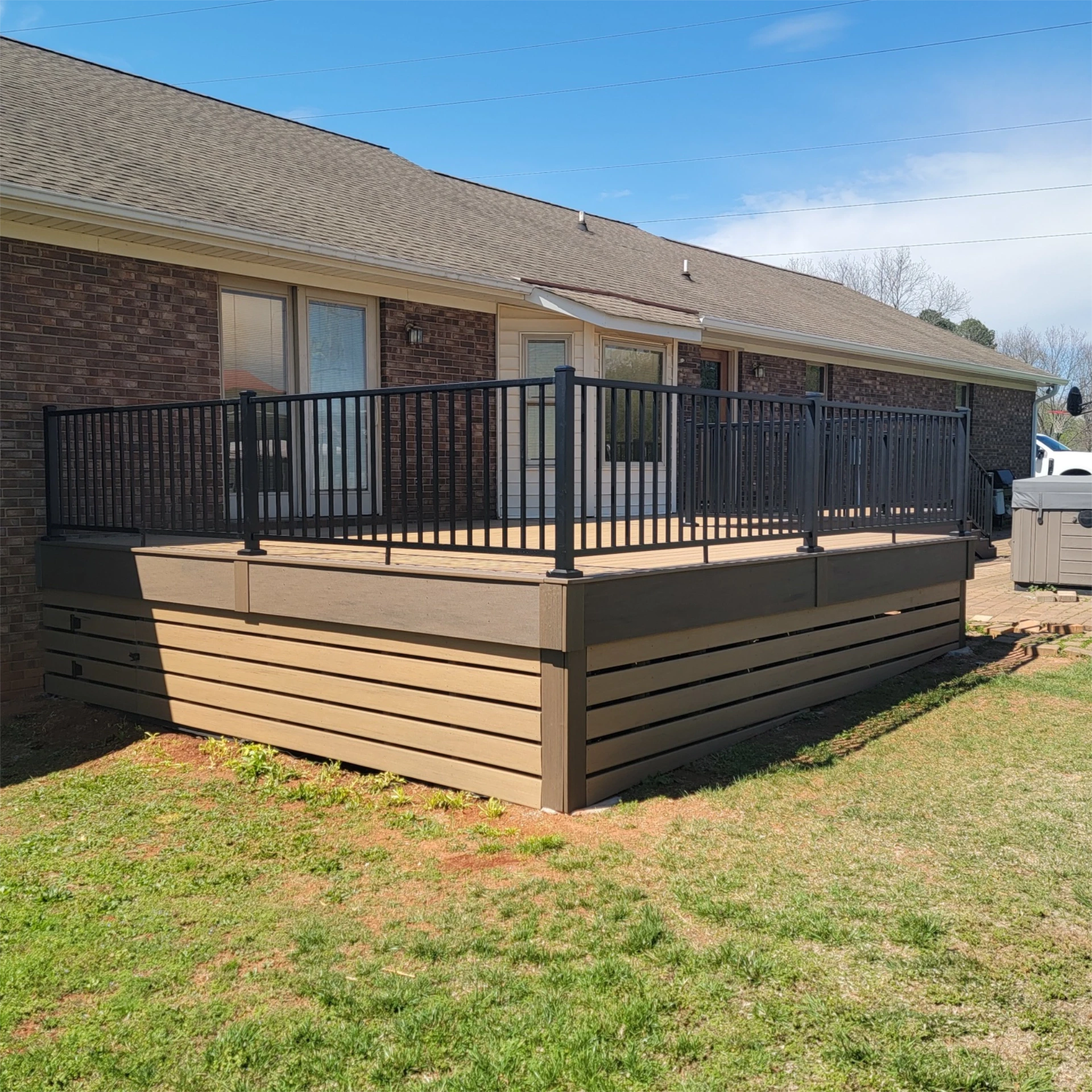 Large tan composite deck with black railing and enclosed skirting.