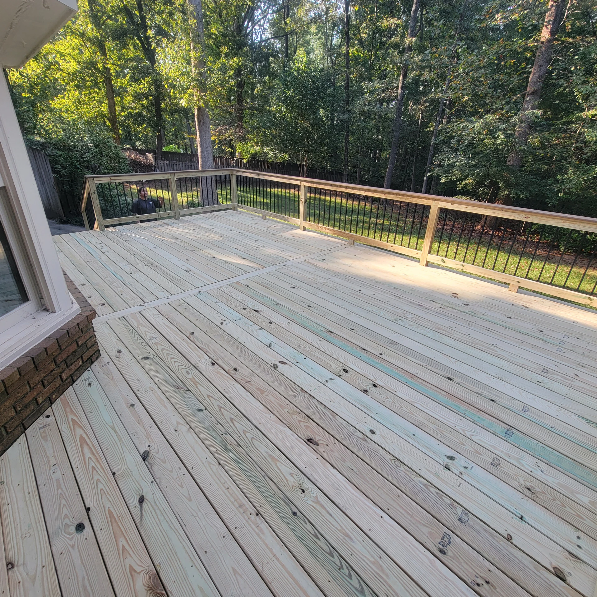 Large unfinished wood deck with black metal railing overlooking a wooded backyard.