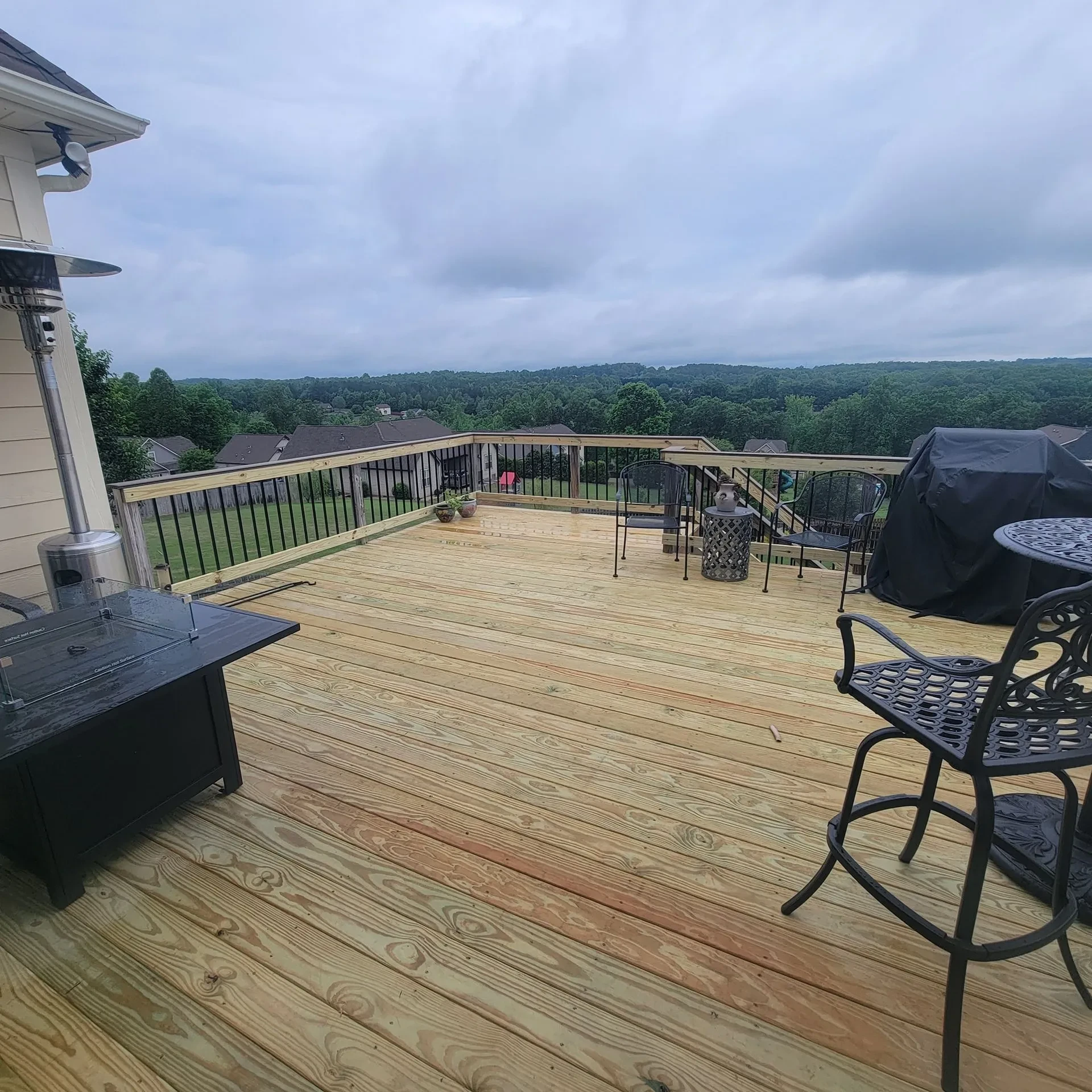 Large wooden deck overlooking wooded hills under cloudy sky.