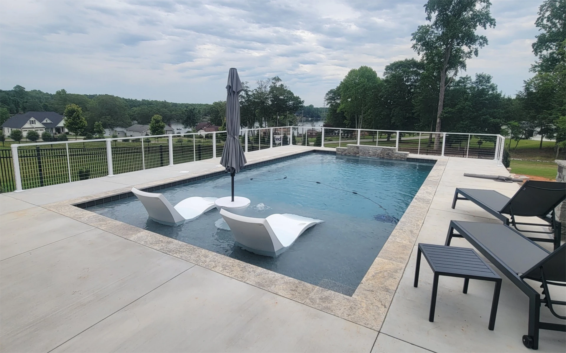 Modern backyard pool with sun shelf, loungers, and lake view.