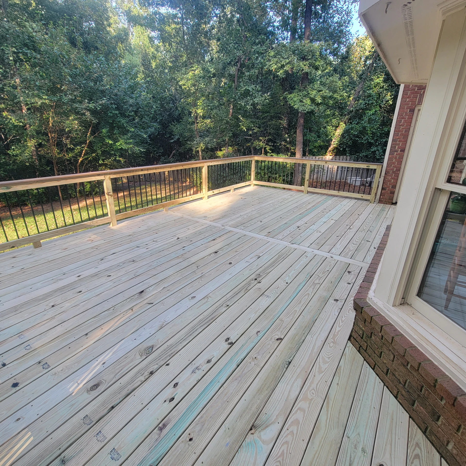 Spacious unfinished wood deck overlooking a wooded yard.