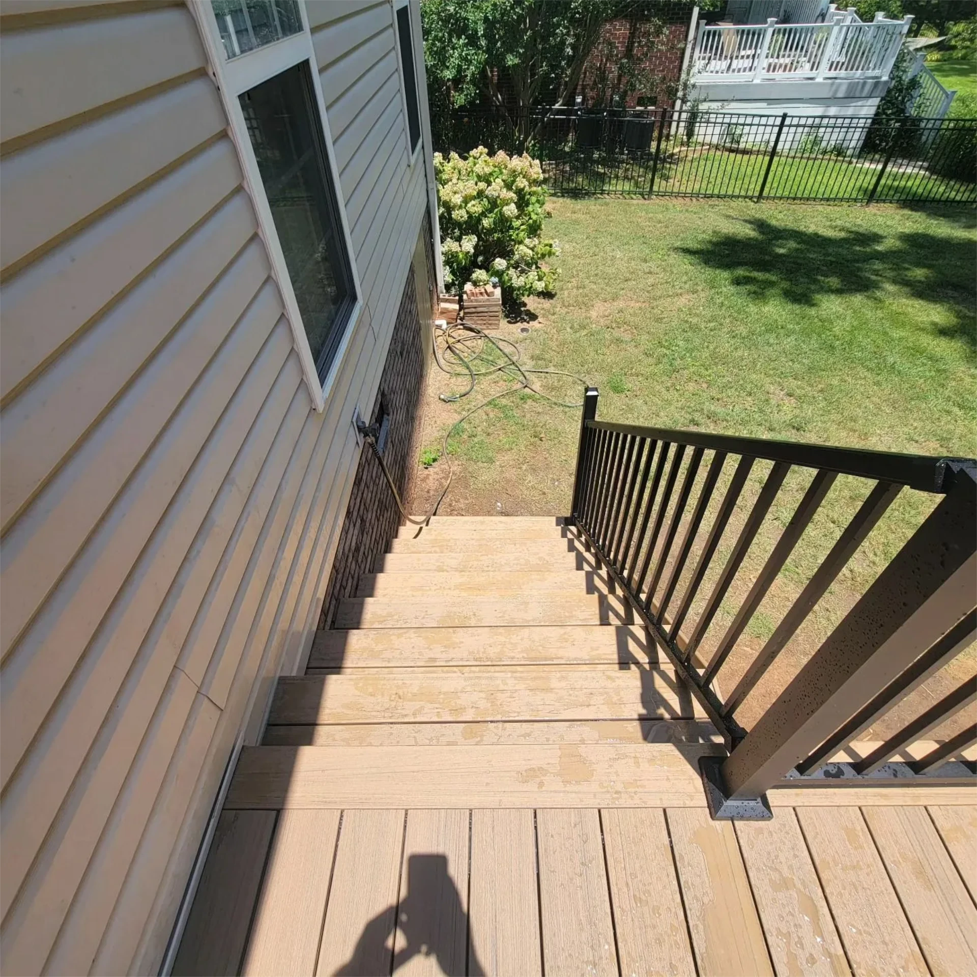 Aerial view of a deck wooden stairs with black railing leading to backyard