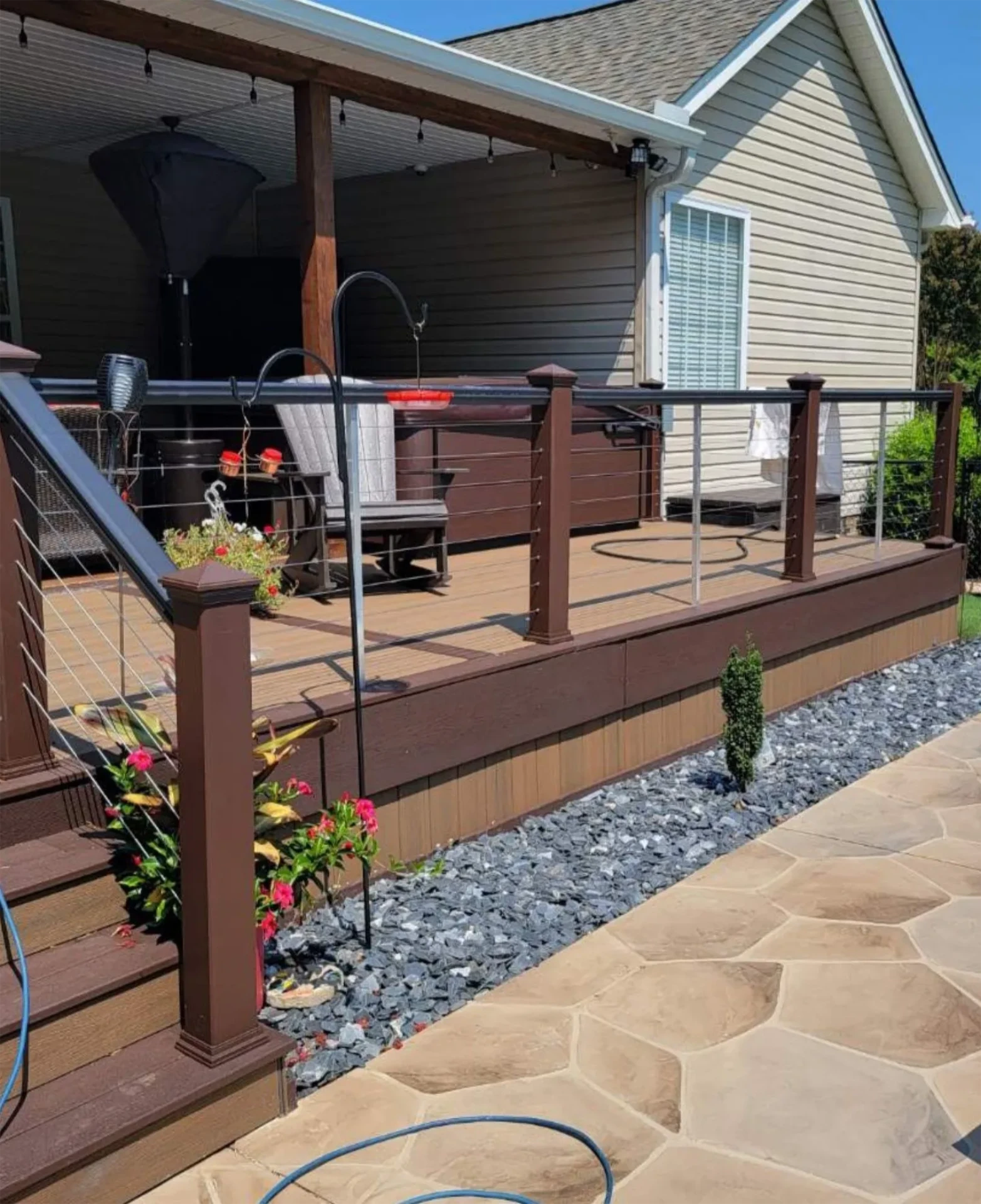 Brown composite wide deck and wooden stairs with cable railing beside stone patio