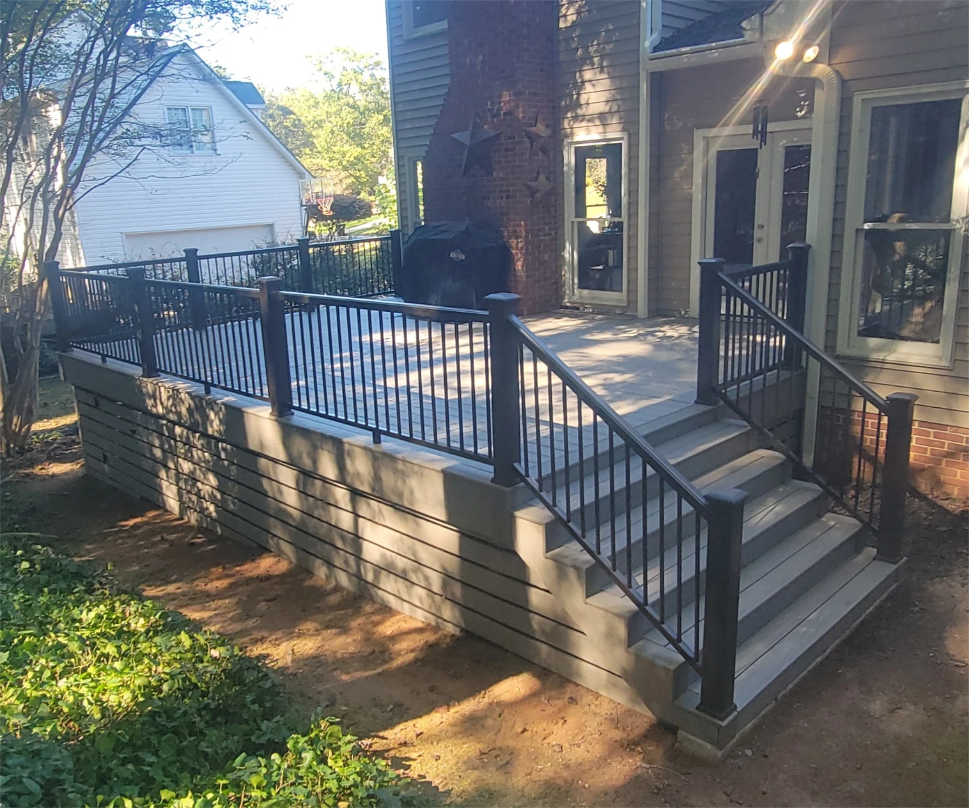 Elevated composite deck with black metal railing and stairs in the sand