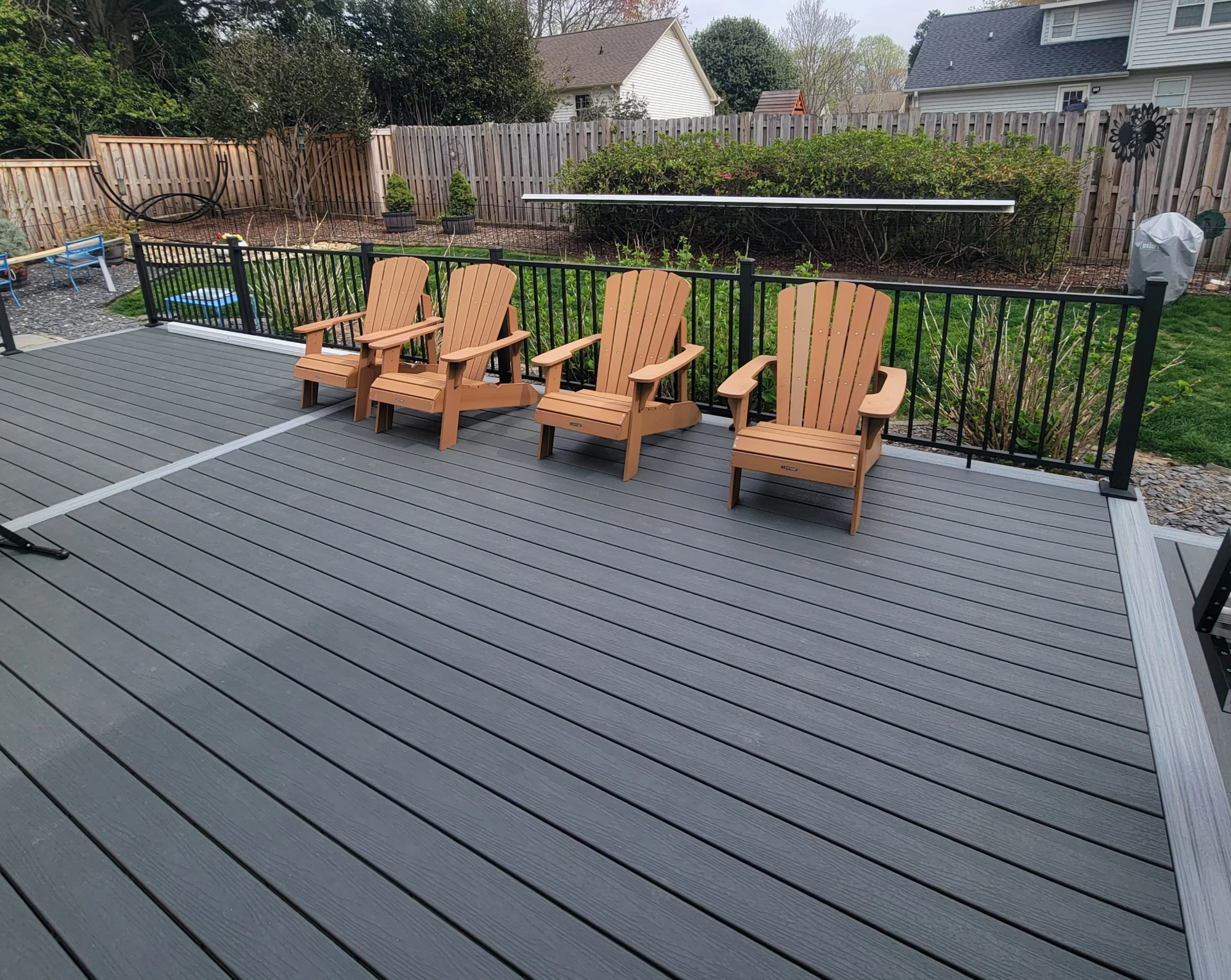 Large gray composite deck with black railing and wooden chairs