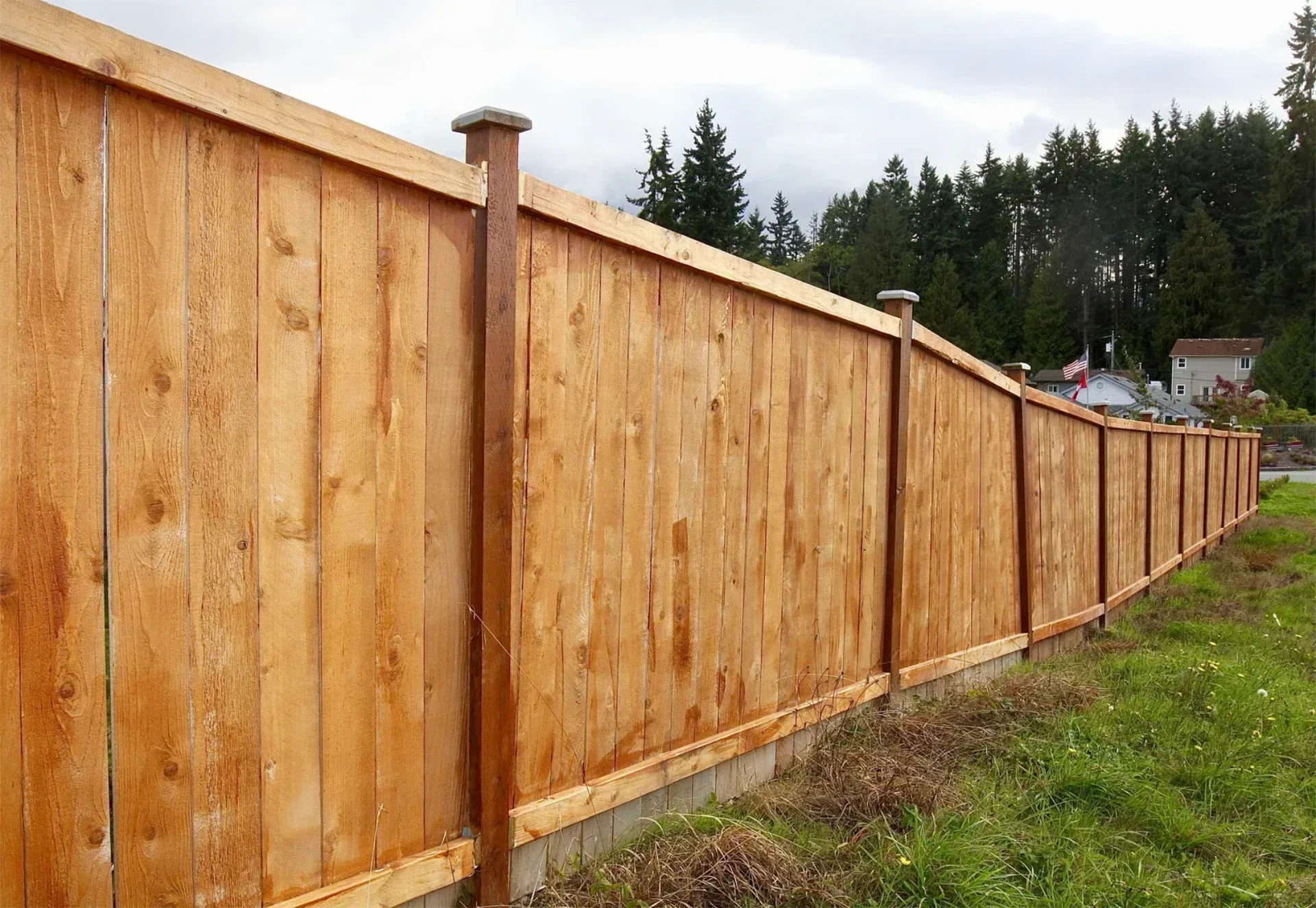 Long cedar privacy fence installation with capped posts on the grass