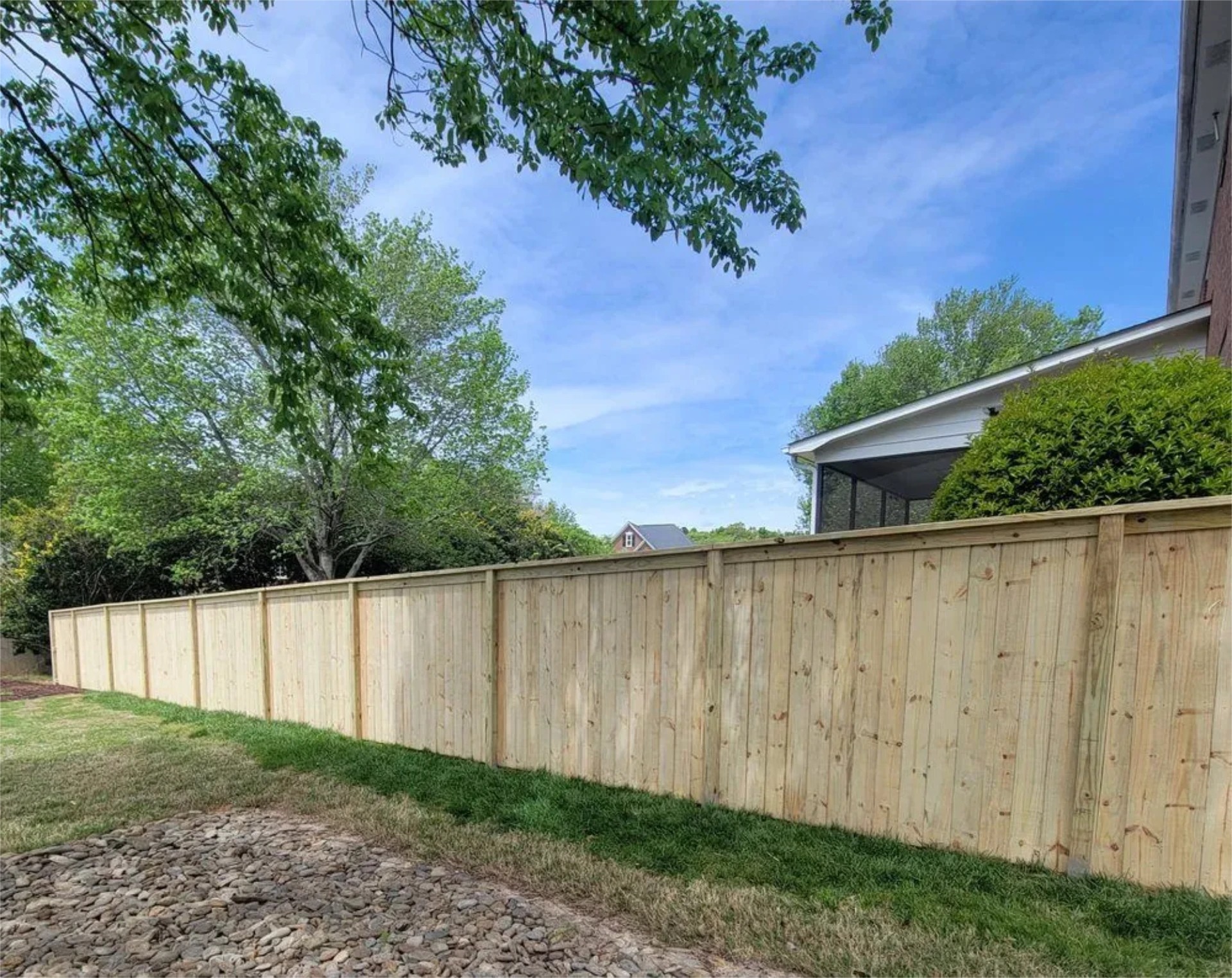 Long wooden privacy fence beside a backyard on the grass with a clear sky view