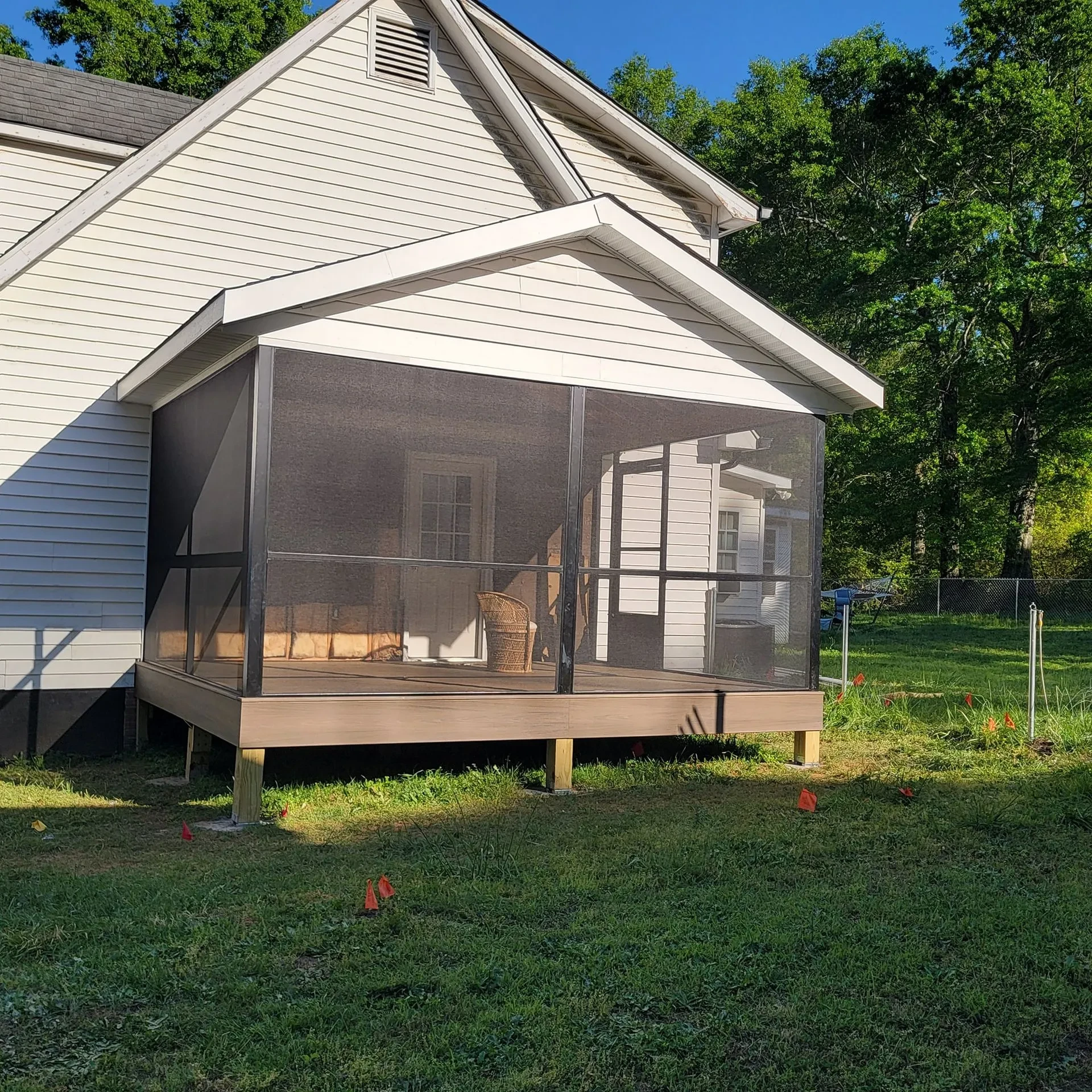 Screened porch attached to a white house with wooden deck on a grassy yard