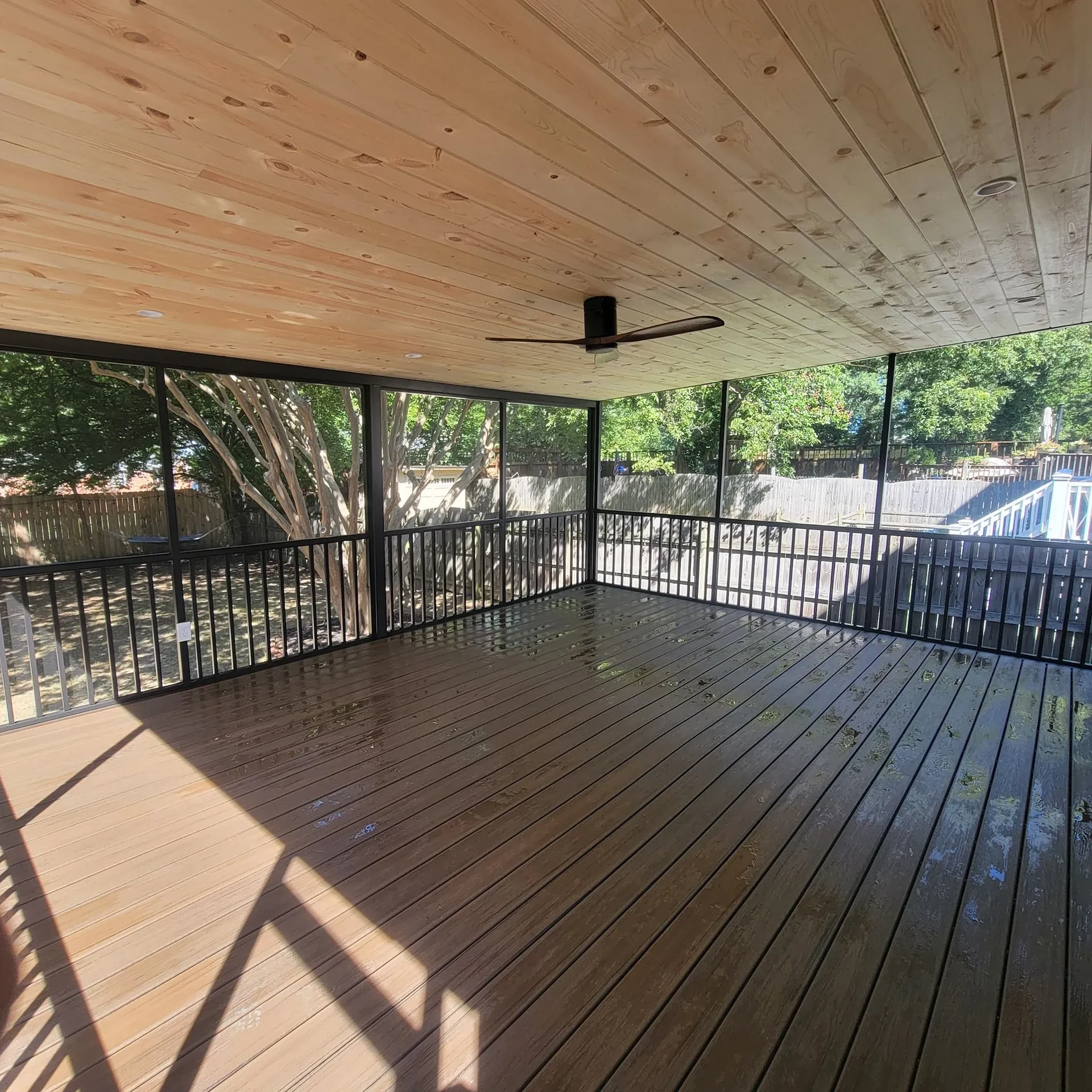 Spacious screened porch with wood ceiling ceiling fan and dark large composite flooring and overlooking view