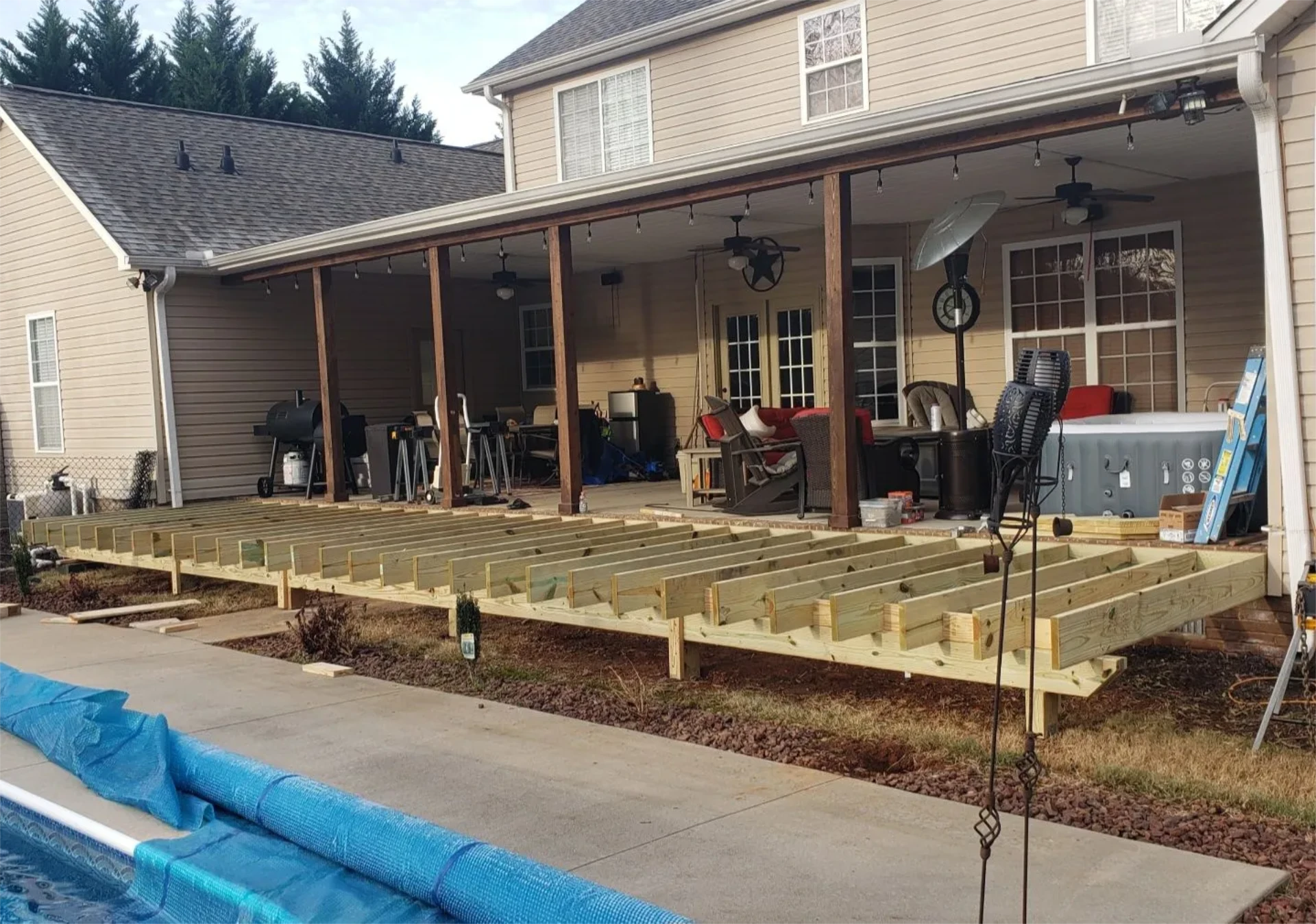Unfinished wooden deck framing beside covered patio and pool