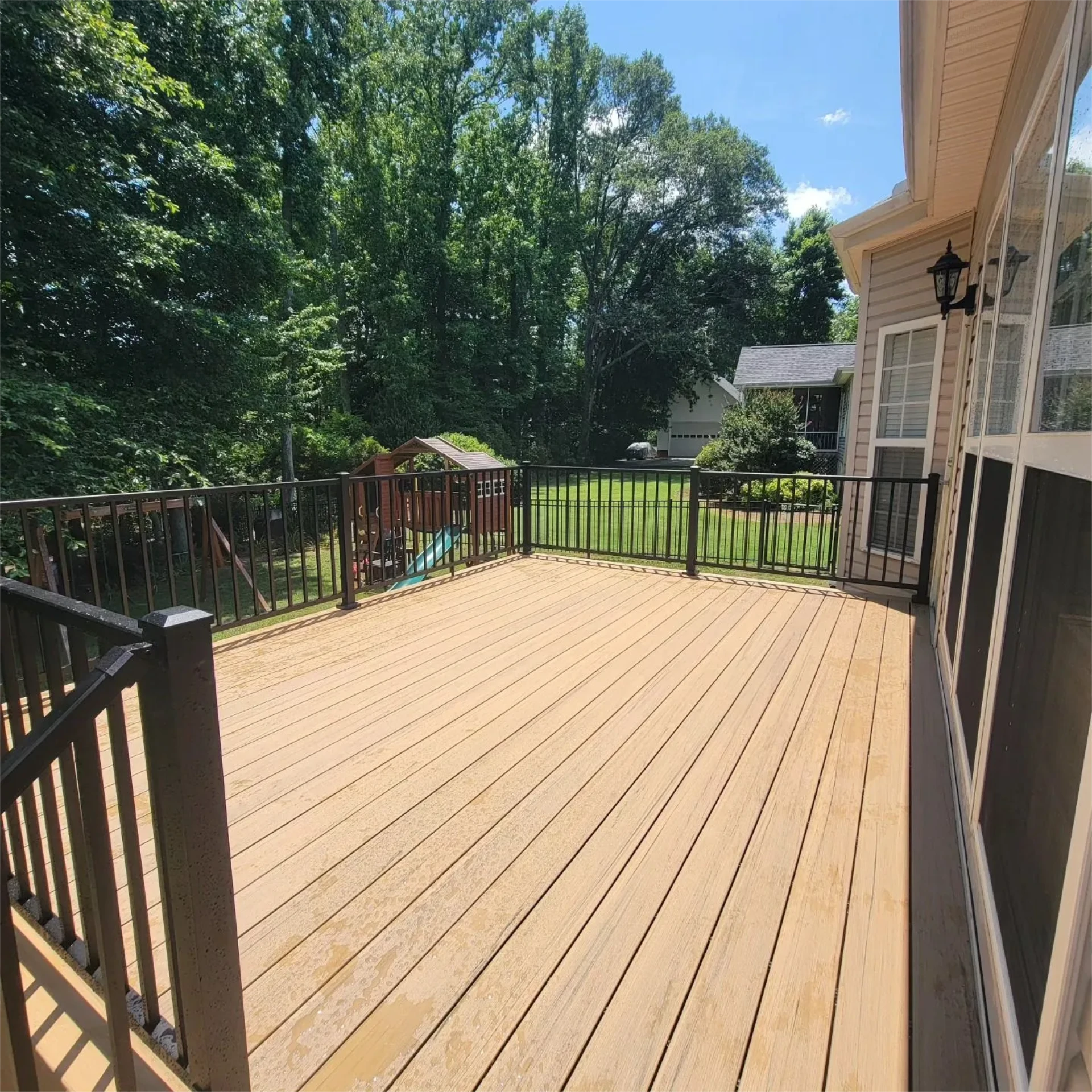 Wide clean composite deck with black metal railing in backyard