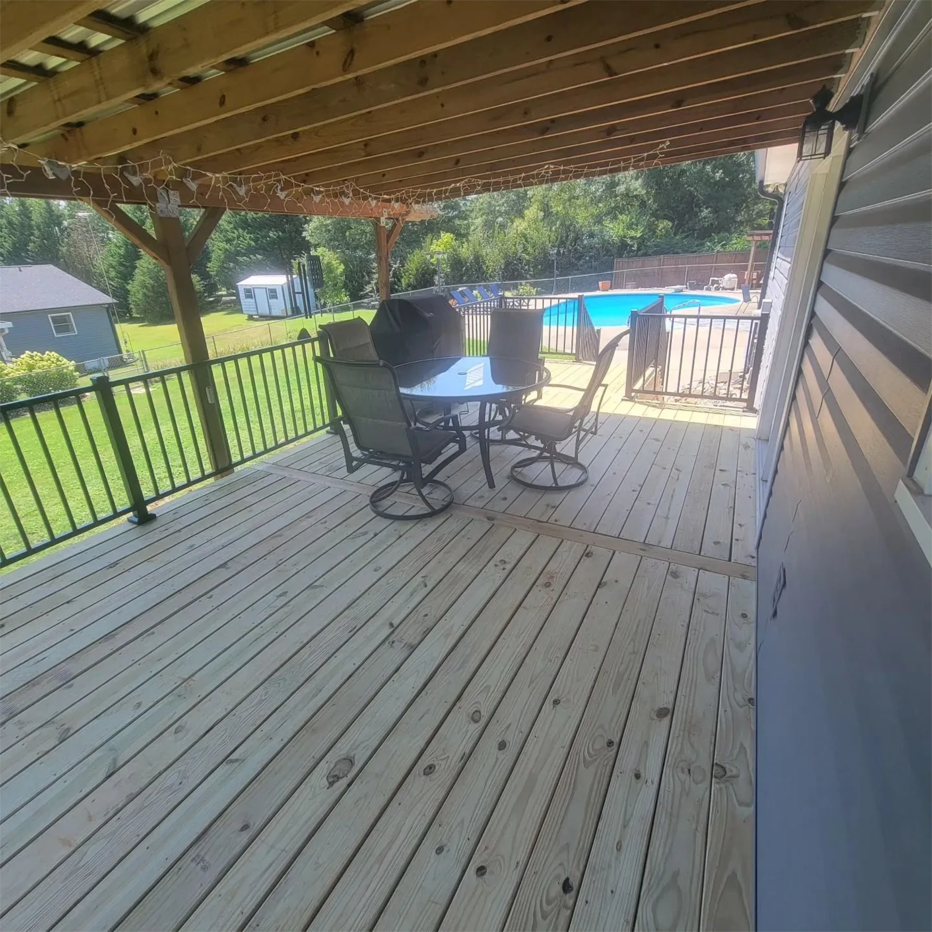 Wooden covered deck with stairs and black railing on a overlooking backyard pool